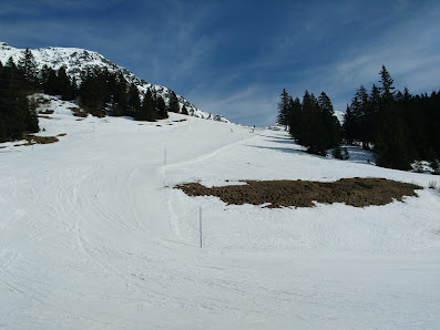 View of a picturesque chalet in Sant Bernardino Switzerland with a ski resort and winter sports centre in the background. Skiers can be seen enjoying winter sports.