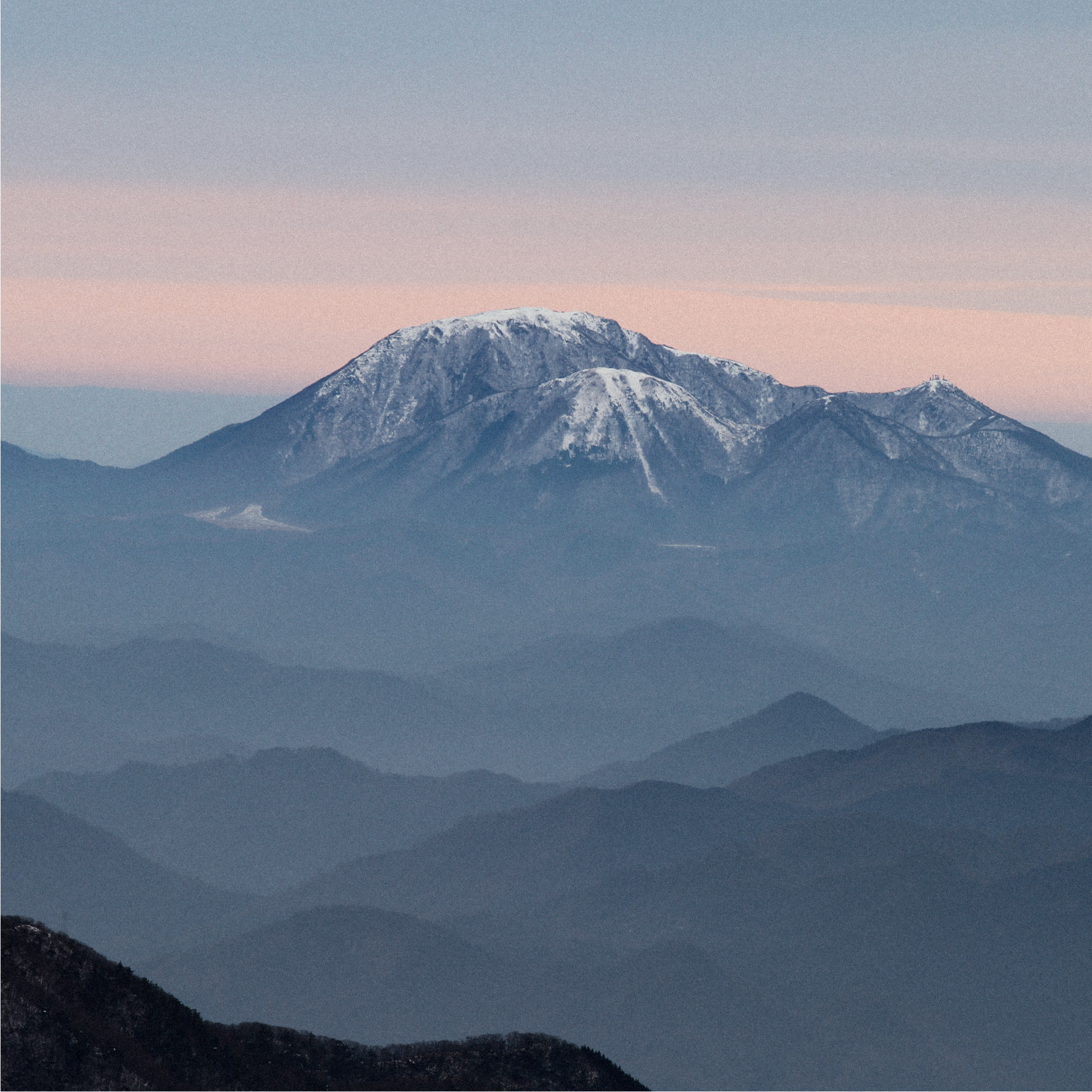View of the majestic mountain at Mizuho Highland in Honshu, Japan, lightly dusted with snow, with a small challet and a mountain bike in the foreground.