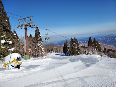 Ski lifts ascending through a lively winter sports scene at Mizuho Highland ski resort in Japan, with skiers and a snowboarder elegantly navigating the powdery slopes.