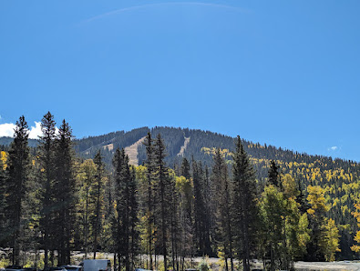 A scenic view of Santa Fé in New Mexico with a mountain backdrop. A ski resort is visible in the distance with a ski lift and winter sports enthusiasts adding to the lively winter scene. A serene lake adds tranquility to this picturesque landscape.