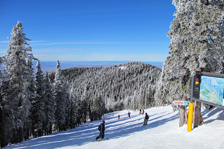 Winter sports scene at a ski resort in Santa Fé, New Mexico, featuring a ski lift in use and a skier gliding down the snowy landscape.