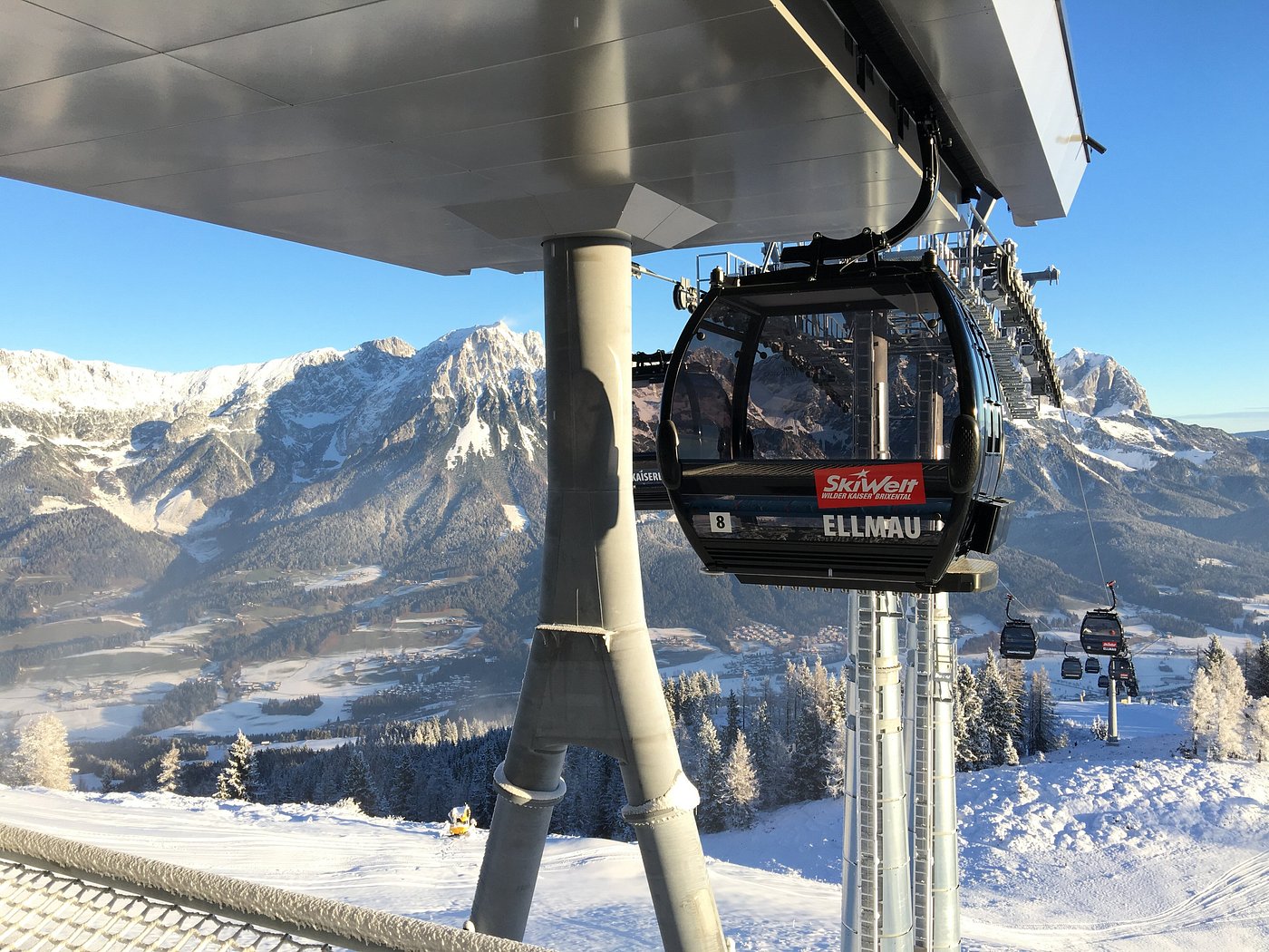 Ski lift ascending a snow-covered mountain at SkiWelt Brixental in Austria, with a rustic chalet to one side and a skier in the distance, showcasing a lively winter sports scene.