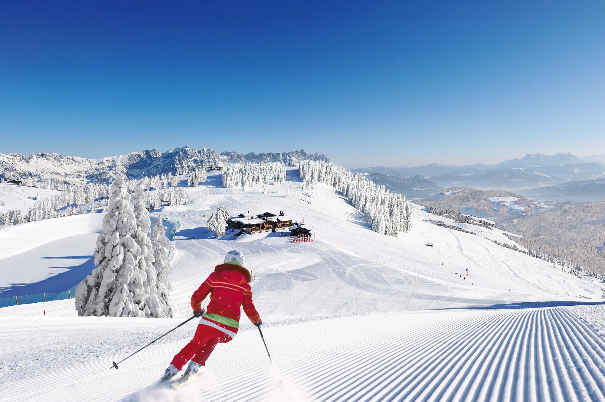 Winter sports enthusiasts enjoy a day at SkiWelt-Brixental ski resort in Söll, Tyrol, Austria, with a skier in action and a ski lift visible in the back.