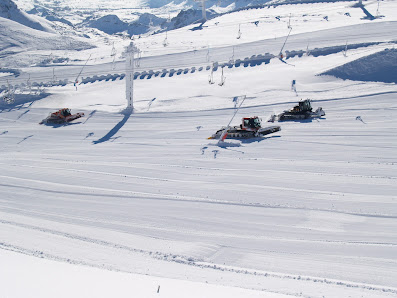 Winter scene at Valgrande-Pajares station in Spain, showcasing a sports centre and ski resort with a charming chalet. A snowmobile is present on the glistening snow, indicating winter sports activity.