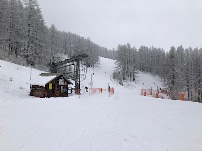 Winter view of the ski resort in Abriès, France, featuring a ski lift, snow-covered slopes, and a challet amidst a lively winter sports scene.