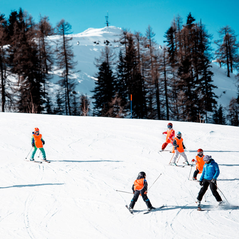 Image showcasing a winter sports scene in Piana di Vigezzo Italy featuring a group of people and a family enjoying skiing activities at a ski resort.