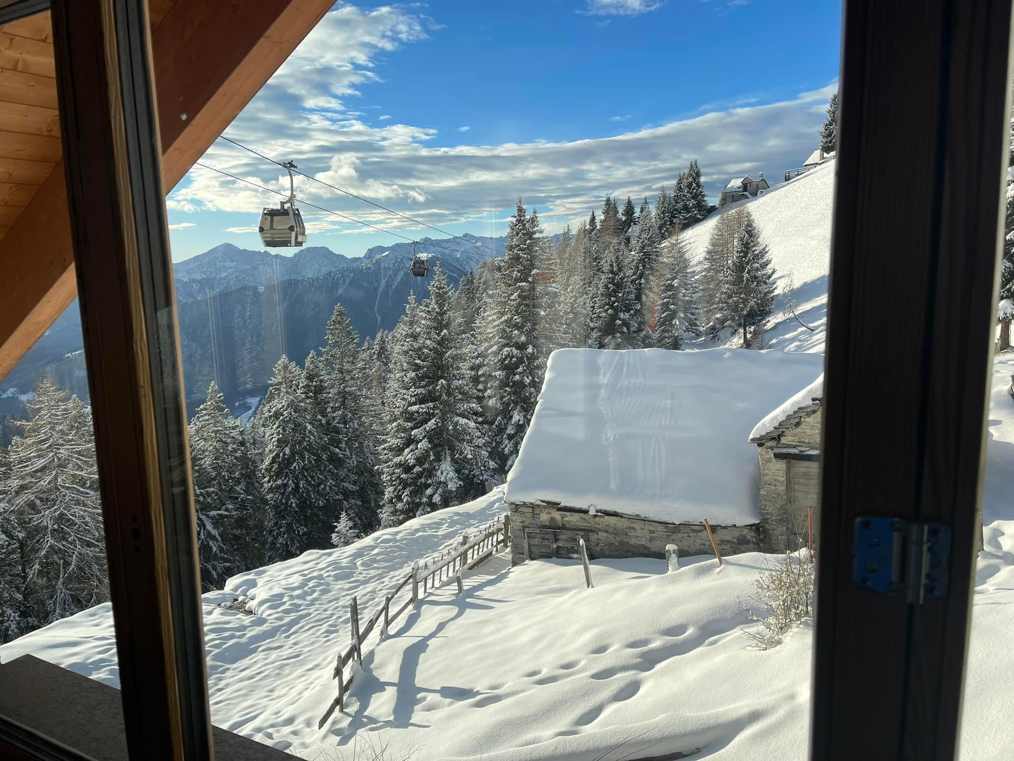 A scenic view in Piana di Vigezzo Italy featuring a ski resort with a ski lift ascending towards a cozy mountain hut and challet amidst a winter sports scene.