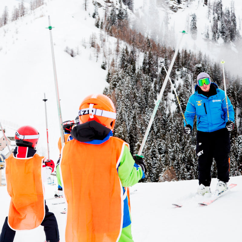 A fun-filled winter sports scene at Piana di Vigezzo in Italy featuring a ski resort. A skier is visible with a family and a group of people enjoying skiing amidst the snowy landscape.