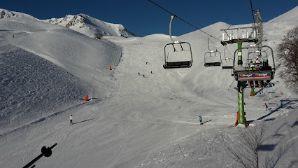 Skier descending a slope at Monte Magnola – Ovindoli, a ski resort in Abruzzo, L’Aquila, Italy. A challet and a ski lift are visible in the backdrop, portraying a classic winter sports scene.
