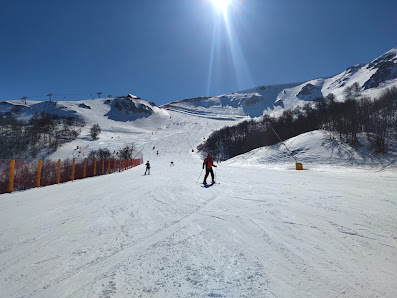 Image showcasing a winter scene at Monte Magnola in Ovindoli Italy. A chalet is in view with a skier in action at the forefront. The overall setting suggests a bustling ski resort.