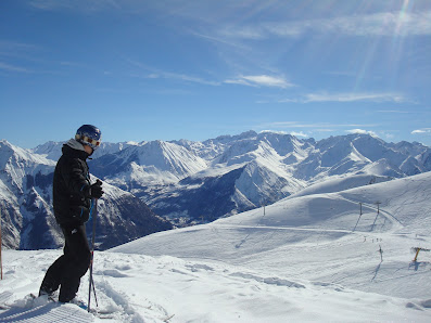 A skier swooshing down an expanse of powdery snow at Luz Ardiden ski resort in France, a charming chalet perched on the nearby hill, providing a picturesque backdrop for this vibrant winter sports scene.