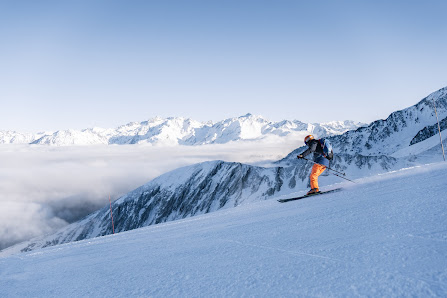 A skier enjoying a winter sports scene at Luz Ardiden ski resort in Argelès-Gazost, Grust, France, with a challet in the distance and a snowboarder nearby.
