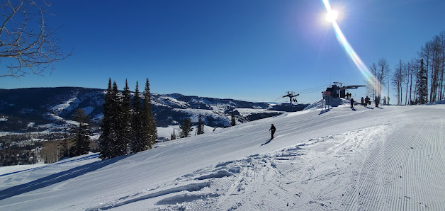 Beaver Mountain ski resort in Garden City Utah bustling with winter sports activity. Skiers glide down snowy slopes a few ride a ski lift beside a cozy chalet nestled at the base.