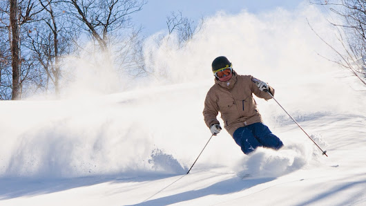 A skier dominates the image carving through the fresh snow at Beaver Mountain Utah. The winter sports scene is alive with activity and excitement. The ski resort stands against a backdrop of snow-covered trees framing an inspiring landscape.