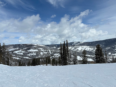 Winter sports scene at Beaver Mountain Ski Resort in Garden City, Utah. A skier descends a snow-covered slope while others ride the nearby ski lift.