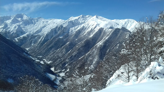 A scenic winter view at Guzet-Neige in Ariège, France, featuring a majestic mountain with a quaint chalet nestled into its slope. There's a ski resort in the distance with skiers enjoying winter sports.