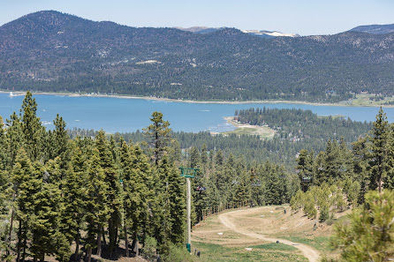 View of Snow Summit ski resort in Big Bear Lake California with a ski lift over a bustling winter sports scene. A lake and mountain bike enhance the natural beauty of the locale.
