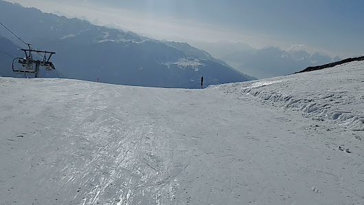 A skier on a piste at the Mont-Noble ski resort in Switzerland, with a charming chalet and spectacular mountain backdrop creating an idyllic winter sports scene.