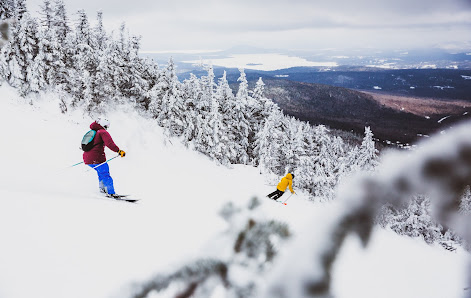 A lively winter sports scene at Saddleback in Rangeley Maine featuring a skier and a snowboarder. The ski resort is blanketed in snow providing a perfect setting for family skiing.