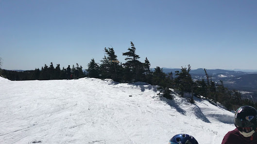 A skier on a snowy trail at Saddleback a ski resort in Rangeley Maine. Majestic mountains make up the background and a ski lift can be slightly visible in this winter sports scene.