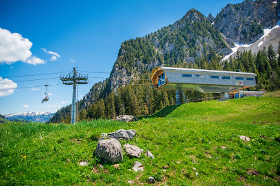 A ski lift ascends towards the top of a mountain at the Jaun-Gastlosen Bergbahnen ski resort in Switzerland with a challet and mountain hut nestled nearby.