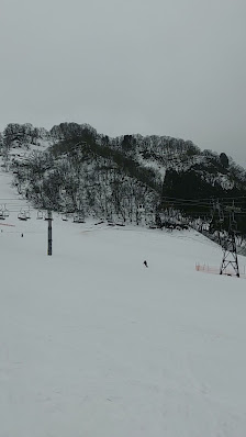 Winter scene at Hakusan Ichirino in Chūbu, Japan, featuring a snow-covered landscape at a bustling ski resort, people enjoying winter sports and a charming challet next to a ski lift.