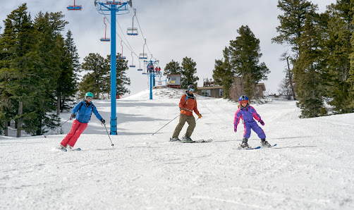 A winter sports scene at Sandia Peak New Mexico with a ski lift in the background. A family and group of people are skiing down the slopes of the ski resort.