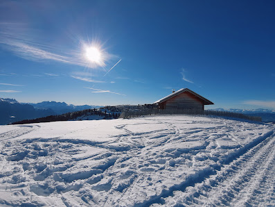 View of the snow-covered Rittner Horn in South Tyrol, Italy, featuring a bustling winter sports center, where skiers enjoy the slopes. A cozy chalet peeks from the corner, adding to the winter charm.