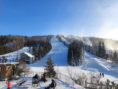 Winter sports enthusiasts enjoying a day at Le Relais Ski Resort in Lac-Beauport, Quebec, Canada, featuring a panoramic view of snow-covered slopes, a distant ski lift, and stunning winter scenery.