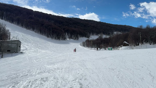 A skier enjoys a run on the snowy slopes of Tsaghkadzor ski resort, Armenia with a charming challet and a ski lift in the background, depicting a bustling winter sports scene.