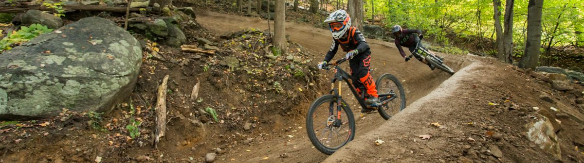 A mountain biker navigating a trail at Mountain Creek - Vernon amidst lush greenery with a distant chalet adding charm to the scene in Vernon Township New Jersey.