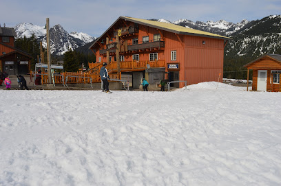A ski resort at The Summit at Snoqualmie in Washington showcasing a bustling winter sports center amidst a scenic winter landscape complete with a charming chalet and an active skier.