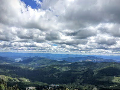 View of a sunny day at Mt. Spokane Ski & Snowboard Park in Mead, Washington, with a mountain landscape in the background, accompanied by a ski lift and resort, nearby a lake.