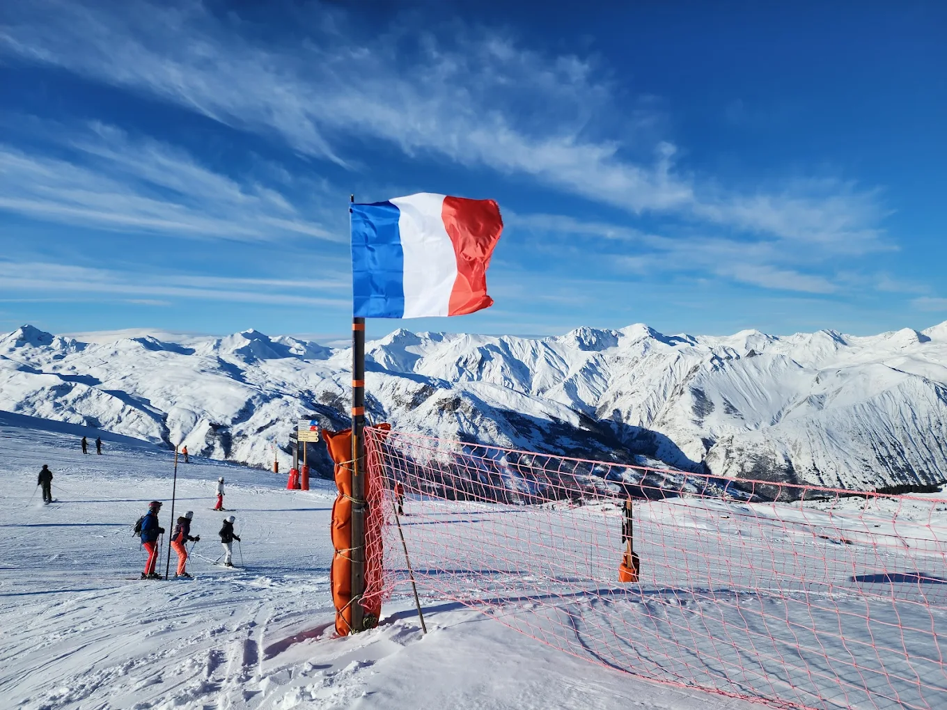 A skier navigates a snowy slope in Les 3 Vallées, France, with hints of a winter sports scene. Possibly, a child learning to ski and a snowboarder can be seen in the distance.