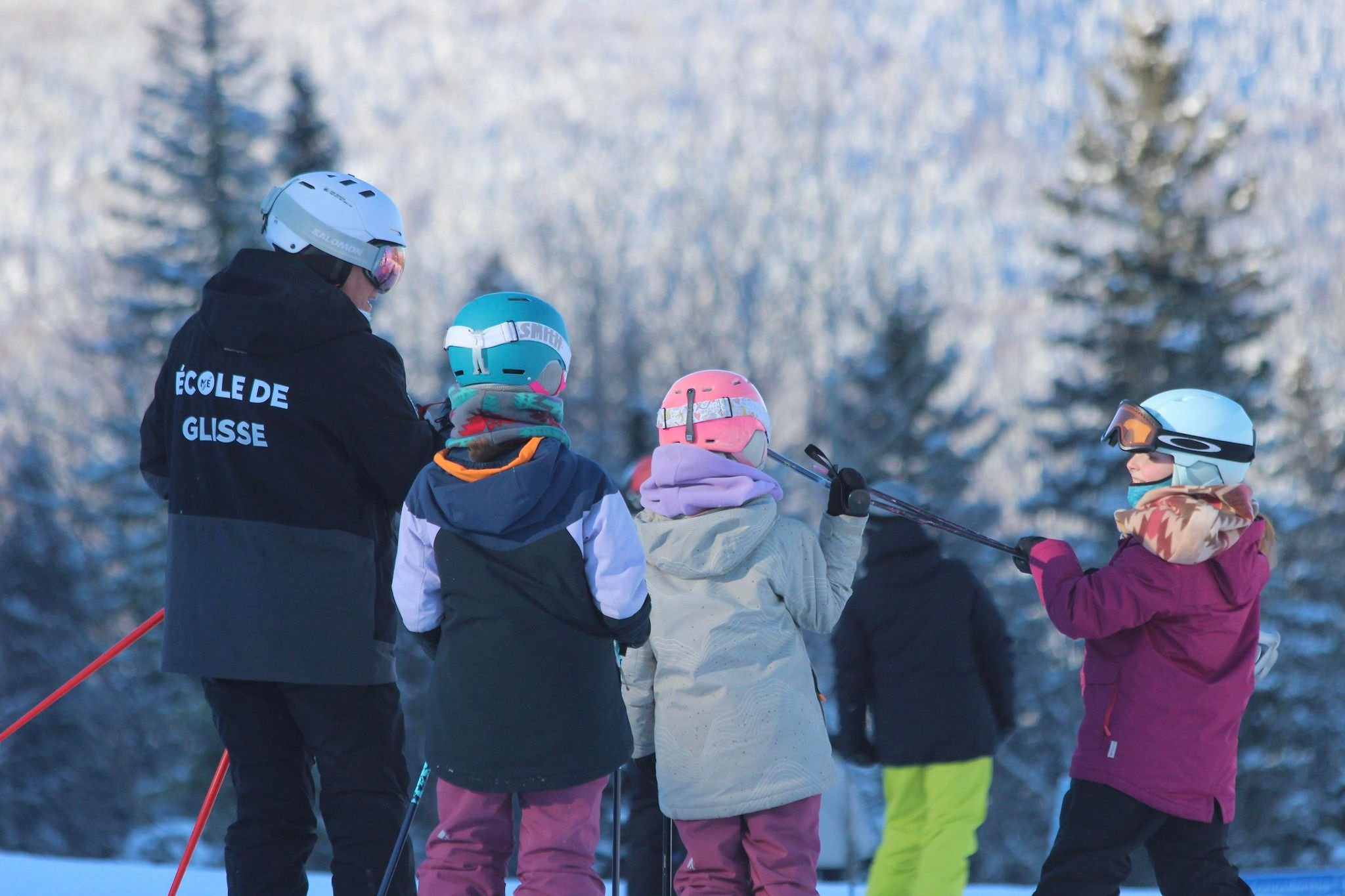 A family enjoying a day of skiing during winter at Mont Edouard L'Anse-Saint-Jean Quebec with the view of a chalet and a winter sports centre in the background.