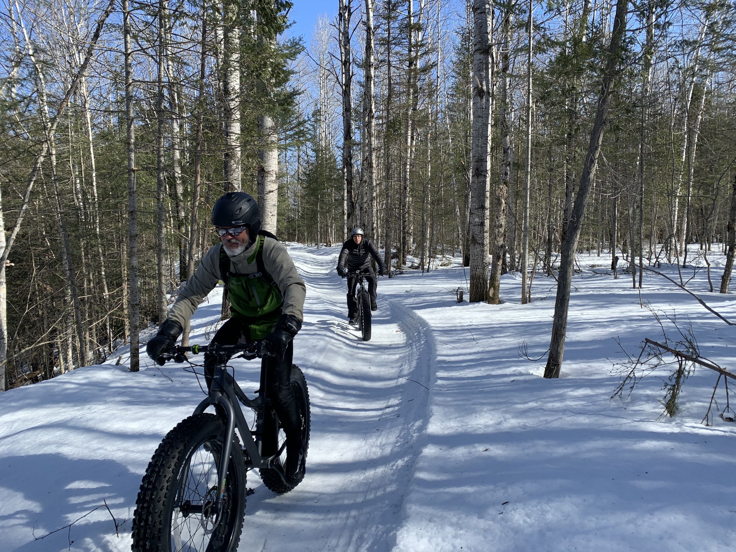 Winter sports scene at Mont Edouard in Quebec, Canada, featuring a mountain bike, a challet, and distant hints of a skier and snowmobile.