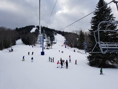 A charming chalet at the lively Pats Peak ski resort in Henniker New Hampshire surrounded by a bustling winter sports scene with a ski lift visible.