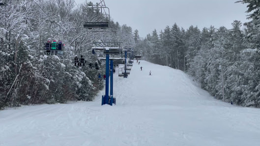 A vibrant winter sports scene at Pats Peak, Henniker, NH, featuring a ski lift in action, a bustling ski resort surrounded by stunning winter scenery, and skiers enjoying the slopes.