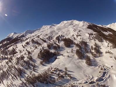 Winter scene at Sainte-Anne la Condamine ski resort in France, showcasing a charming chalet, activity on the snow-covered slopes, and majestic mountain backdrop.