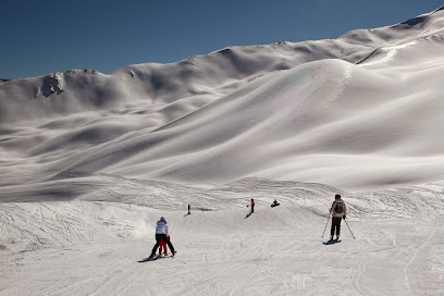 A winter sports scene at Sainte-Anne la Condamine ski resort in France with a group of skiers on the slope amidst beautiful white landscape and a cozy chalet in the backdrop.