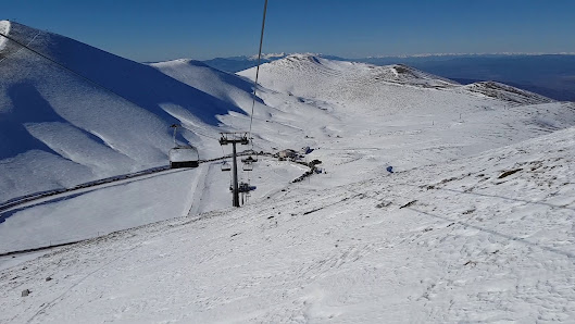 A scenic view of Falakro Ski Resort in Greece featuring a ski lift amidst a lively winter sports scene. A charming chalet and winter sports centre add to the excitement of the snowy landscape.