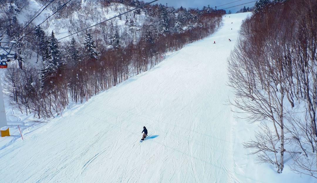A skier gliding down the slopes at Sapporo Kokusai - Jozankei Kogen ski resort in Hokkaido, Japan, amidst a stunning winter scene. A ski lift can be faintly seen in the background.