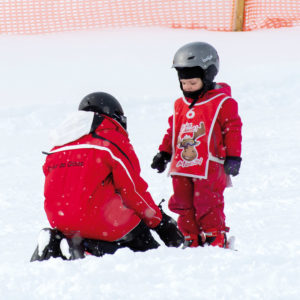 Skier enjoying a sunny day at Mont Orignal in Quebec, Canada. A winter sports centre and chalet sit nearby as a child learns to ski in this winter wonderland.