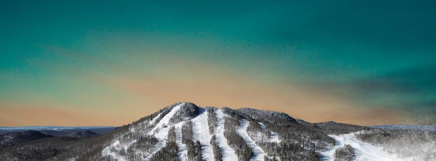 A scenic view of Mont Orignal Ski Resort in Quebec Canada. The landscape features a skier making their way down the snowy mountain against a backdrop of beautiful winter scenery.