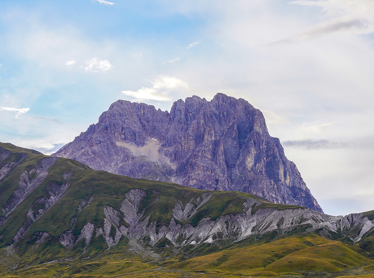 Gran Sasso in Italy - a mountain range with green grass and mountains in the background.