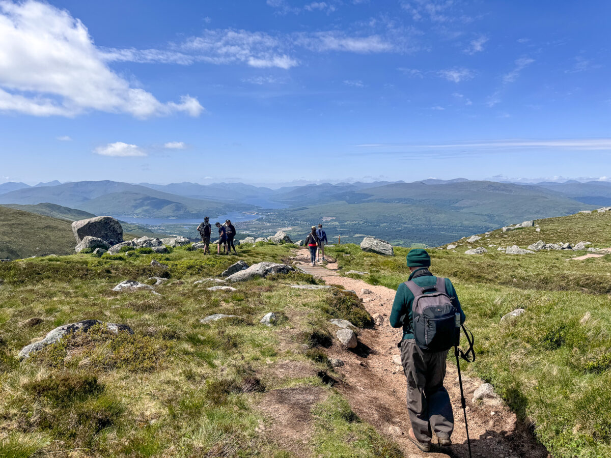 Sunlit view of Nevis Range in the Highlands, Scotland with a quaint challet and a lodge nestled at the foot of the towering mountain. A mountain bike suggests adventure on this beautiful day.