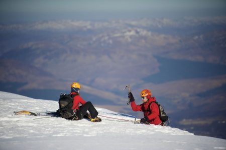 A skier and a snowboarder participating in winter sports at the Nevis Range in Torlundy, Fort William, Scotland. The scene captures the spirit of a ski resort in the Highlands.
