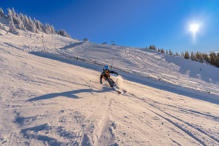 A skier and snowboarder navigate a winter sports scene at La Dôle | ​Les Tuffes in France. A chalet in the distance and other aspects of the ski resort sprinkle the snowy landscape.