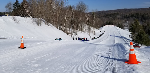 A bustling winter sports scene at Titus Mountain in The Adirondacks Malone New York with a skier in the foreground groups of people skiing and visible structures of a ski resort.