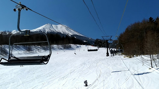 Skiers are enjoying a winter day on a slope at Kaida Kogen Mia ski resort in Nagano, Japan. A ski lift ascends to the mountain while a chalet can be spotted in the background.